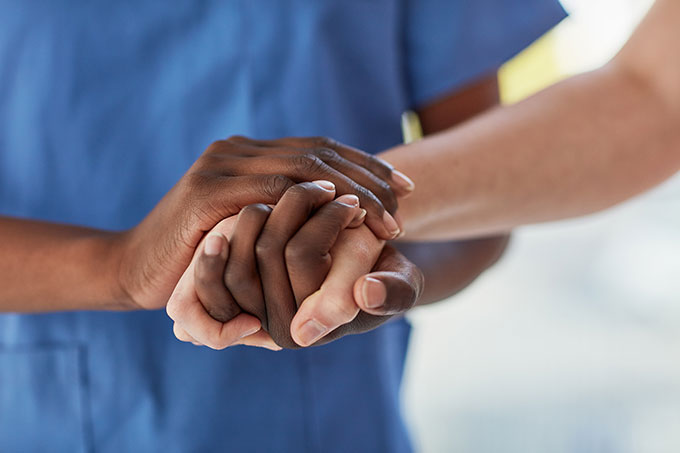 Man in scrubs holding a patient's hand.